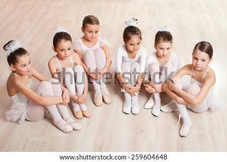 A group of six little ballerinas sitting on the floor gathered around their teacher and listen to advice. They are good friend and amazing dance performers