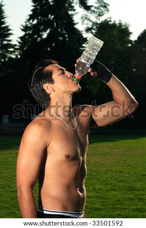 A shirtless man drinking a bottle of water in a field