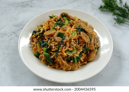 Selective focus Mie Goreng Tek-tek or fried noodles with topping slice meatballs, eggs and mustard greens (caisim or sawi hijau). Served in white plate. Look like noised with fried noodles.  Stok fotoğraf © 