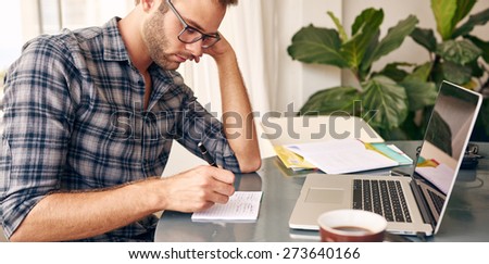 Horizontal image of a businessman writing notes on a writing pad while sitting at his desk behind his new notebook with his morning coffee