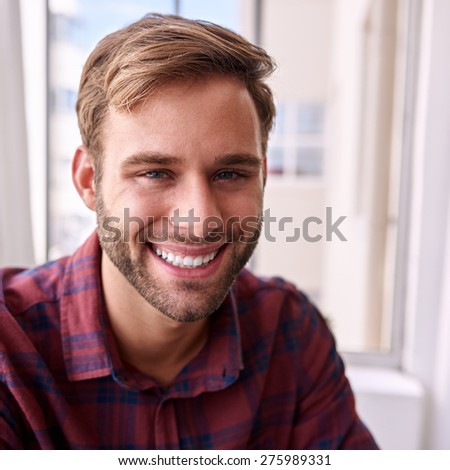 Close up portrait of a happy young entrepreneur smiling at the camera wearing a maroon check shirt