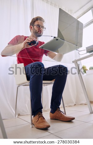 Full body shot of a young student busy working on his laptop computer shot from below through his glass desk, while he works wearing a red shirt with a trimmed beard