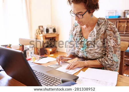 Well aged female bookkeeper busy crunching numbers on her calculator at her desk in her home office