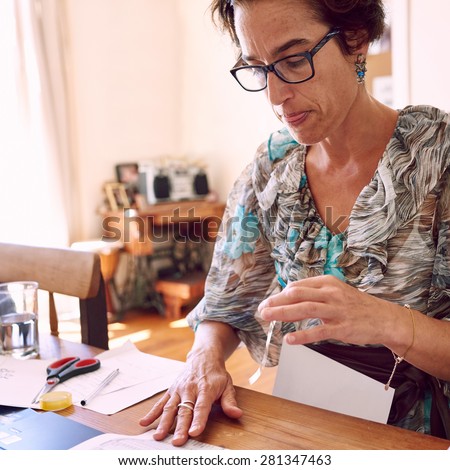 Mature business woman busy taping together pieces of paperwork to file her red tape in her home office as neatly as possible