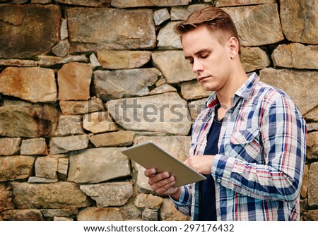portrait image of a successful young entrepreneur with style using his tablet with a grungy stone wall background