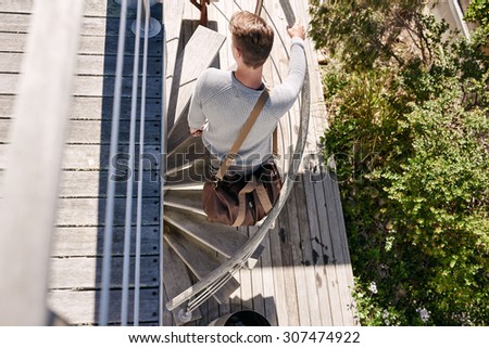 A birds eye perspective of a stylish handsome young man busy climbing up a beautifully designed spiral staircase, while carrying a leather duffel bag over his shoulder
