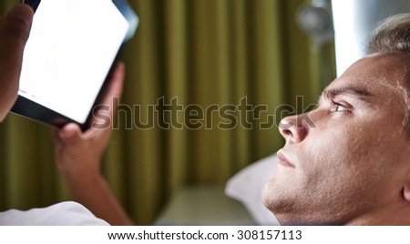 Workaholic businessman is busy reading electronic business reports on his tablet, while lying in bed before going to sleep