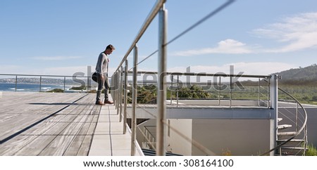 Image of a young business man shot from the side while he walks across a bridge on the rooftop of his modern home