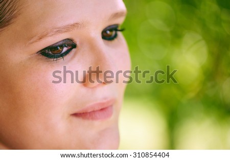 Close up of a soft woman\'s face as she looks down and off camera with beautiful green bokeh for copy space