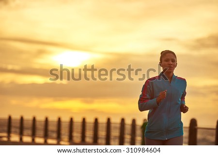 Beautiful sunrise silhouette image of a adult female runner taking a morning jog along the promenade next to the ocean