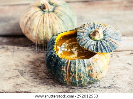Pumpkin soup served in a pumpkin - homemade recipe of cream vegetarian dish swirled with coconut milk on a wooden table.