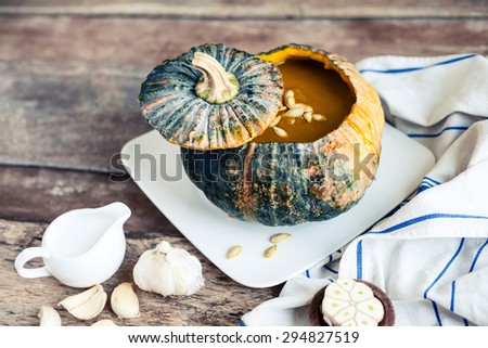Pumpkin soup served in a pumpkin - homemade recipe of cream vegetarian dish swirled with coconut milk on a wooden table.