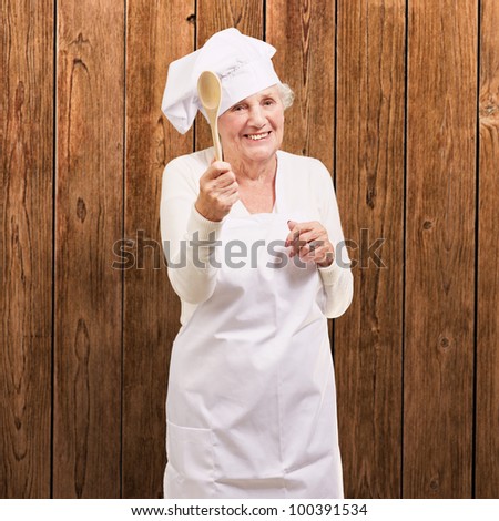 portrait of a senior cook woman holding a wooden spoon against a wooden wall