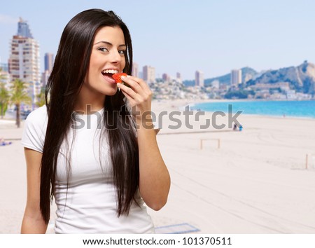 portrait of young woman eating strawberry against a beach