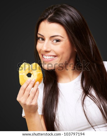 portrait of a young woman eating a donut over a black background