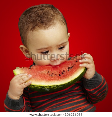 portrait of a handsome kid biting a watermelon over a red background
