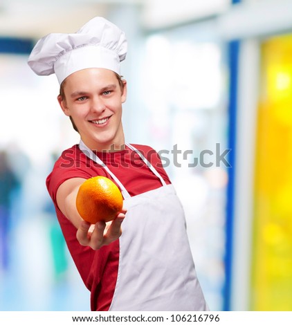 portrait of a young cook man offering an orange indoor