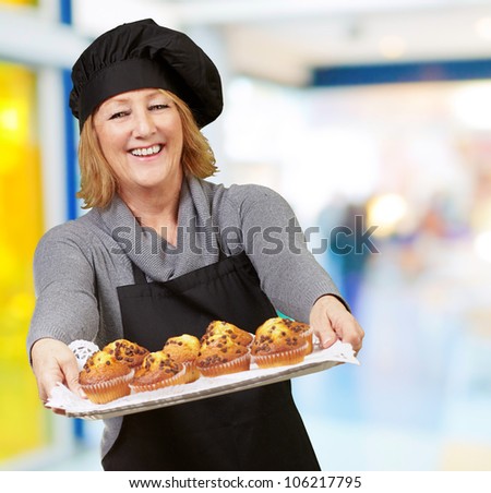 portrait of a cook woman showing a homemade muffins tray at a restaurant