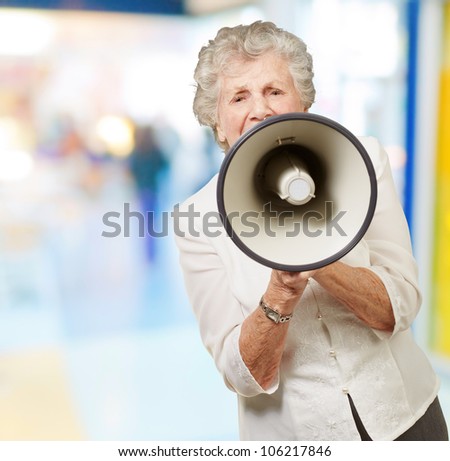 portrait of a senior woman screaming with a megaphone at a crowded place