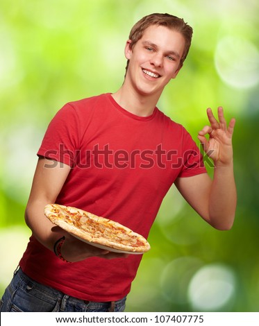 portrait of a young man holding a pizza and doing a good gesture against a nature background