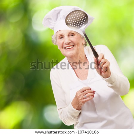 portrait of a sweet senior cook woman holding a metal spoon against a nature background