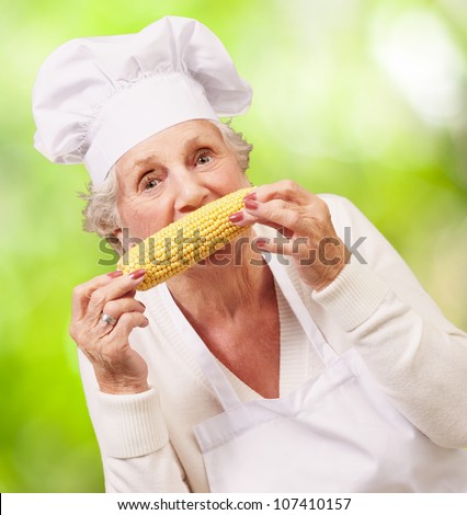 portrait of a senior cook woman eating a corn cob against a nature background