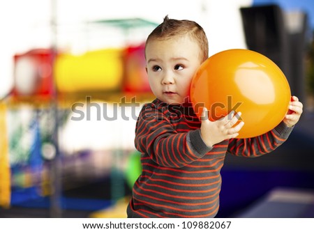portrait of a funny kid holding a big orange balloon against an abstract background