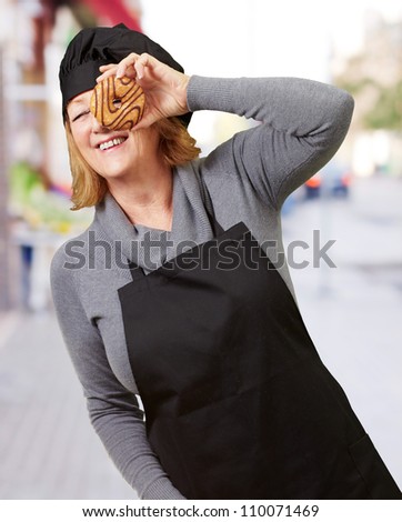 Middle aged cook woman looking through a donut at street