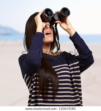 portrait of young woman looking through binoculars against a beach