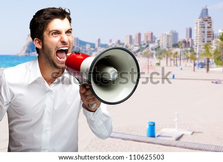 portrait of young man screaming with megaphone against a beach