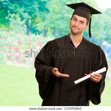 Young Man In Graduation Gown Holding Certificate, Outdoor