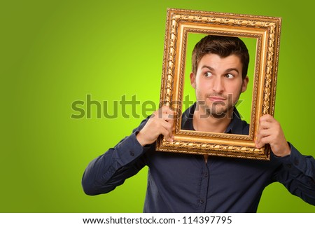 A Young Man Holding And Looking Through Frame On Green Background