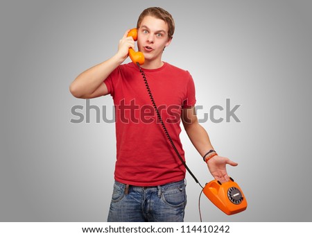Portrait of a young man talking on vintage phone on grey background
