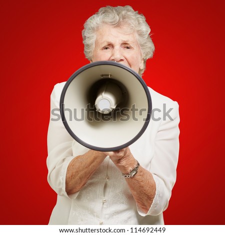 portrait of senior woman screaming with megaphone over red background