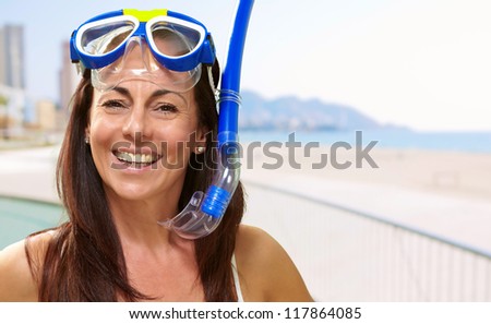 portrait of a happy middle aged woman wearing snorkel and goggles against the beach