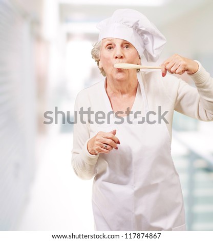 portrait of cook senior woman with wooden spoon on mouth indoor