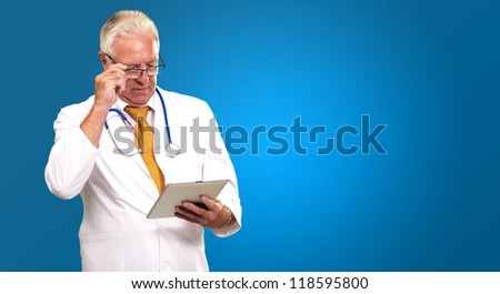 Portrait Of A Male Doctor Holding A Tab On Blue Background