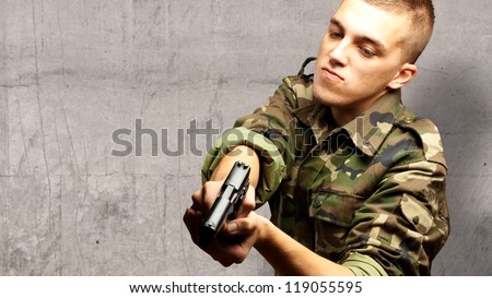 portrait of a serious soldier aiming against a concrete background