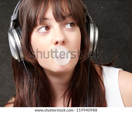 portrait of young woman listening to music with bubble gum against a grunge wall