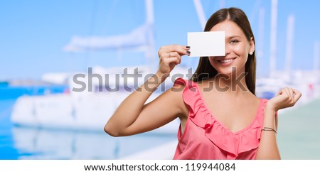 Woman holding a blank placard in front of her eye at a port