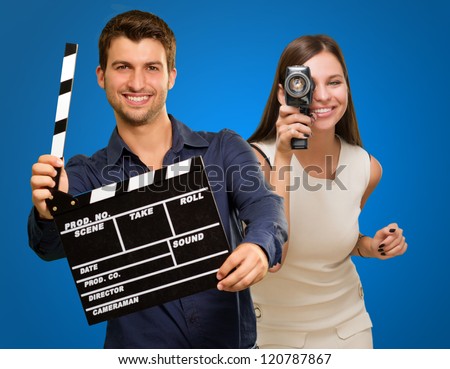 Man Holding Clapper Board And Woman Capturing Photo On Blue Background