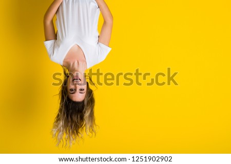 Beautiful young blonde woman jumping happy and excited hanging upside down over isolated yellow background 商業照片 © 