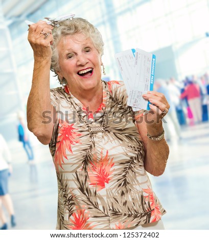 Senior Woman Holding Boarding Pass And Miniature, Indoors