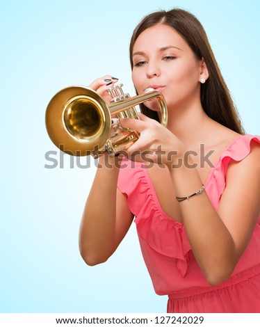 Portrait Of A Young Woman Blowing Trumpet against a blue background