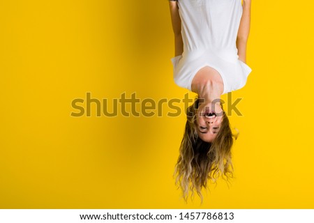 Beautiful young blonde woman jumping happy and excited hanging upside down over isolated yellow background 商業照片 © 