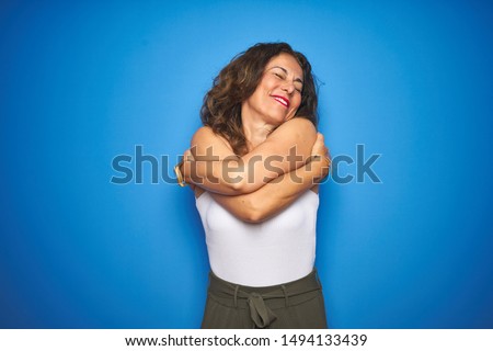 Middle age senior woman with curly hair standing over blue isolated background Hugging oneself happy and positive, smiling confident. Self love and self care Сток-фото © 