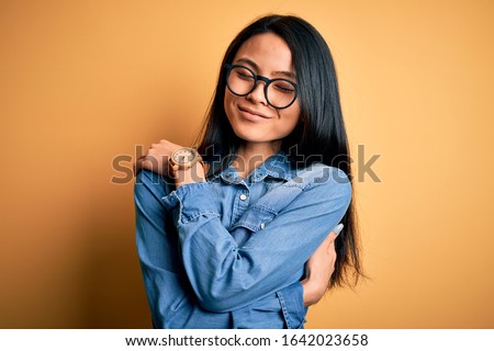 Young beautiful chinese woman wearing casual denim shirt over isolated yellow background Hugging oneself happy and positive, smiling confident. Self love and self care Сток-фото © 