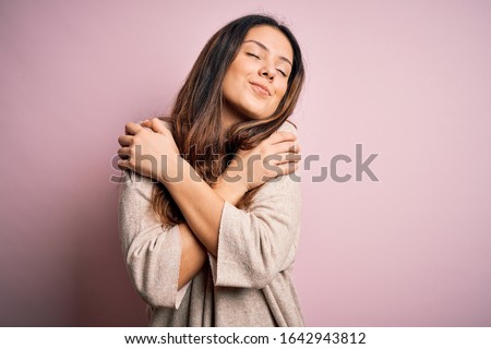 Young beautiful brunette woman wearing casual sweater standing over pink background Hugging oneself happy and positive, smiling confident. Self love and self care Stock foto © 