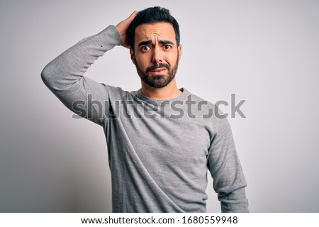 Young handsome man with beard wearing casual sweater standing over white background confuse and wonder about question. Uncertain with doubt, thinking with hand on head. Pensive concept.