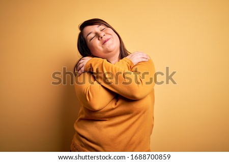 Beautiful brunette plus size woman wearing casual sweater over isolated yellow background Hugging oneself happy and positive, smiling confident. Self love and self care Сток-фото © 